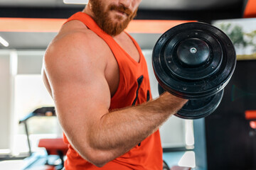 Fototapeta na wymiar Caucasian bearded athletic man with an effort trains with dumbbells in the gym. Close-up of the biceps. Fitness concept