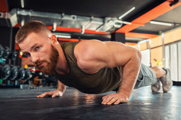 Fototapeta na wymiar Portrait of young bearded athletic man doing push-ups in the gym. Close-up. The concept of fitness and training