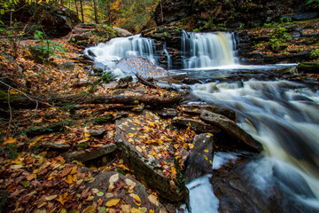Fototapeta na wymiar flowing silky cascading waters with colorful autumn foliage background on the woods in Ricketts Glen Pennsylvania