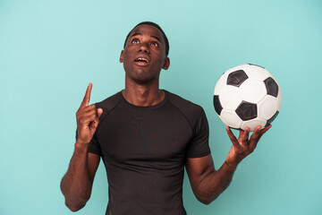 Young African American man playing football isolated on blue background pointing upside with opened mouth.