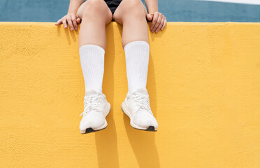 Woman wearing white sports shoes sitting on yellow retaining wall