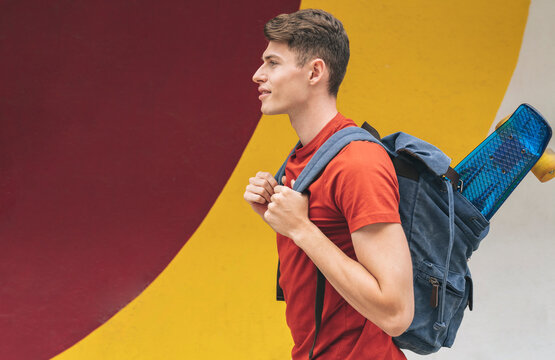 Young man carrying backpack with skateboard in front of wall