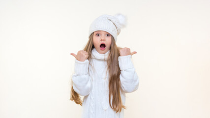 A surprised little girl with her mouth open points her fingers to the sides. isolated background.