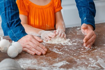 Obraz na płótnie Canvas Little girl cooking food in kitchen with dad. Daddy's hands help children's hands to knead dough. Child daughter with kneads flour dough. Father daughter cooking together 