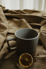 Empty grey coffee cup on beige background isolated while next to it there is a dried plant with a slice of orange. Close-up image.
