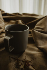 Empty grey coffee cup on beige background isolated while next to it there is a dry plant. Close-up image of a coffee still life.