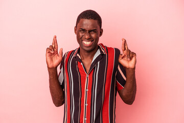 Young African American man isolated on pink background crossing fingers for having luck