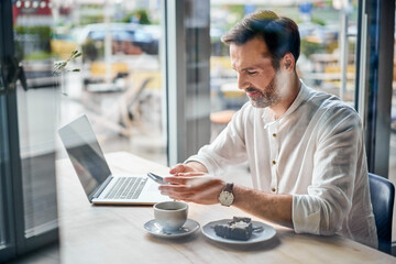 Mid adult man working from cafe using smartphone