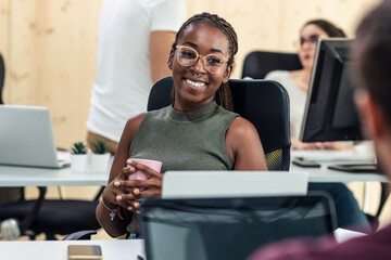 Afro smiling business woman talking with her colleague while working with laptop in a coworking place.