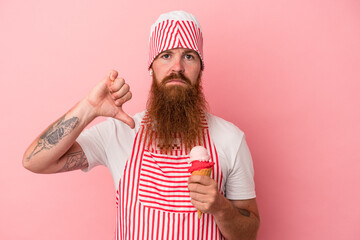 Young caucasian ginger man with long beard holding an ice cream isolated on pink background showing a dislike gesture, thumbs down. Disagreement concept.