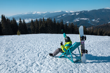 man snowboarder sitting in chair enjoying mountains view