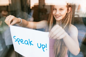 Speak up! paper, young girl showing sign through glass window, the new normal