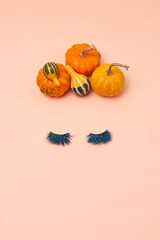 Creative woman face made of eyelashes and pumpkins hair on the orange background. Minimal beauty concept. Flat lay. Helloween makeup creative concept.