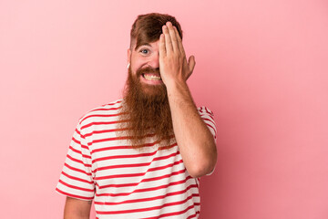 Young caucasian ginger man with long beard isolated on pink background having fun covering half of face with palm.
