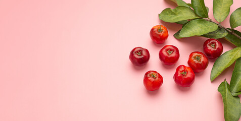 Ripe red acerola cherries fruit and green leaves isolated on a pink background. High vitamin C and antioxidant fruits. Top view. Flat lay. Space for text. Concept of healthy fruits