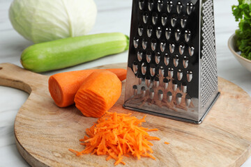 Grater and fresh ripe carrot on wooden board, closeup