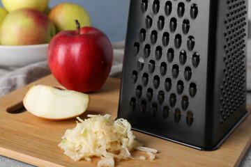 Grater and fresh ripe apple on wooden board, closeup