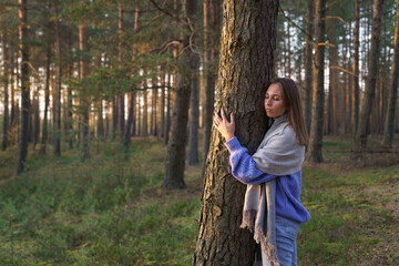 Love and unity with nature: young calm woman hugging tree trunk with closed eyes. Spiritual female...