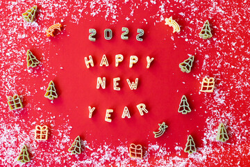 Lettering Happy New Year, christmas trees, gifts and stars made of raw wheat pasta on a red background. Salt as snow. Flat lay, top view. Winter art food concept.