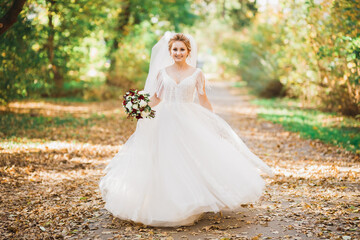 Beautiful bride in elegant white dress holding bouquet posing in park