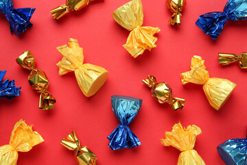 Many candies in colorful wrappers on red background, flat lay