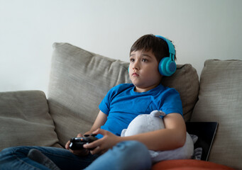 Portrait kid wearing headphones and playing video game. Child holding console play game online at home, Young boy siting sofa having fun and relaxing on his own on weekend