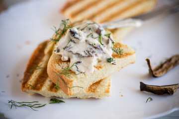 fried bread toast with cheese spread with boiled dried mushrooms on a wooden table.