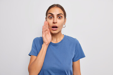 Startled young European woman gasps from wonder keeps hand near face mouth opened spreads rumors...