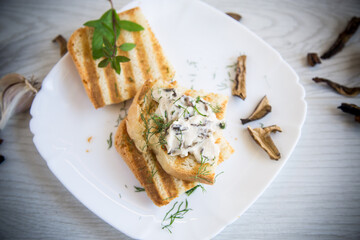 fried bread toast with cheese spread with boiled dried mushrooms on a wooden table.