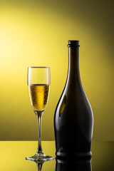 tall champagne glass next to bottle with highlights on yellow background