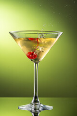 cocktail martini with cherries and splash with splashes in a glass on a green background