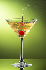 cocktail martini with cherries and splash with splashes in a glass on a green background