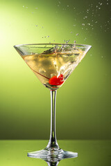 cocktail martini with cherries and splash with splashes in a glass on a green background