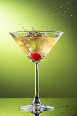 cocktail martini with cherries and splash with splashes in a glass on a green background