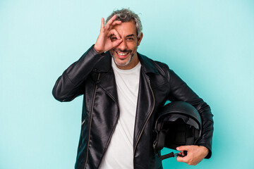 Middle age biker caucasian man holding helmet isolated on blue background  excited keeping ok...