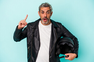 Middle age biker caucasian man holding helmet isolated on blue background  having an idea,...