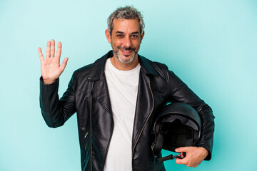 Middle age biker caucasian man holding helmet isolated on blue background  smiling cheerful showing number five with fingers.