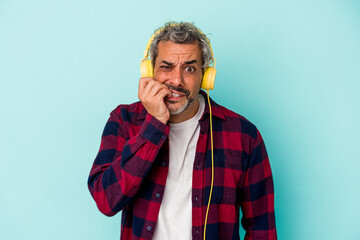 Middle age caucasian man listening to music isolated on blue background  biting fingernails, nervous and very anxious.