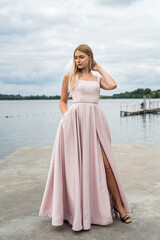Fototapeta na wymiar Young woman in long pink evening dress standing alone near lake at city park