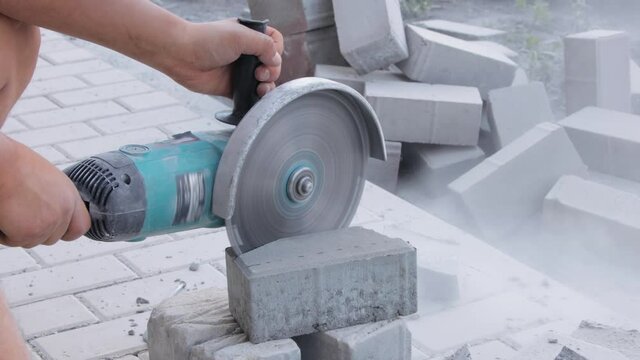 Worker cutting paving stone with angle grinder