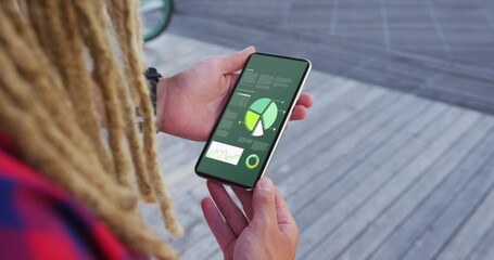 Hands of caucasian man with dreadlocks using smartphone with statistics on screen