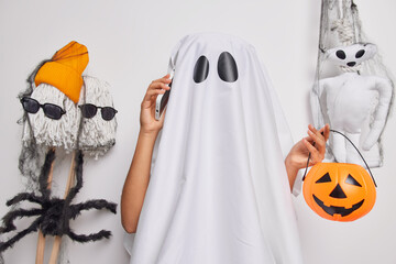 Spooky ghost holds carved orange pumpkin calls friends via smartphone invites for halloween party...