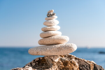 Pyramid stones on the seashore on a sunny day on the blue sea background. Happy holidays. Pebble beach, calm sea, travel destination. Concept of happy vacation on the sea, meditation, spa, calmness.