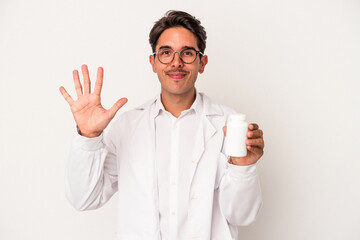 Young pharmacist mixed race man holding pills isolated on white background smiling cheerful showing...
