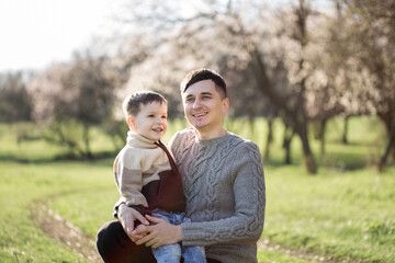 Portrait of a father and son in knitted sweaters on the background of a flowering tree in spring.