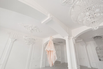 Fototapeta na wymiar Luxurious peach wedding dress hangs on a chandelier in a white room