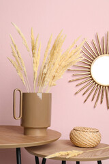 Stylish ceramic vase with dry flowers on wooden table near pink wall