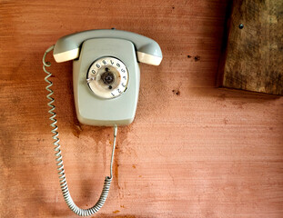 Light gray analog phone with cracked dial and dirty coiled cord hangs on pink painted stained wall