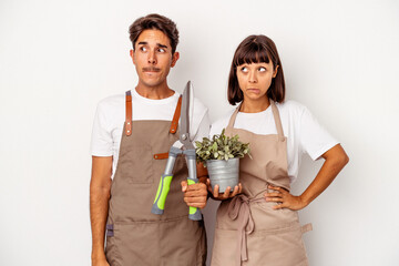 Young mixed race gardener couple isolated on white background confused, feels doubtful and unsure.