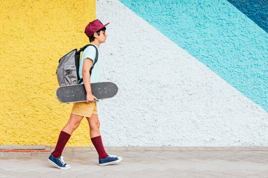Boy with backpack and skateboard walking by multi colored wall